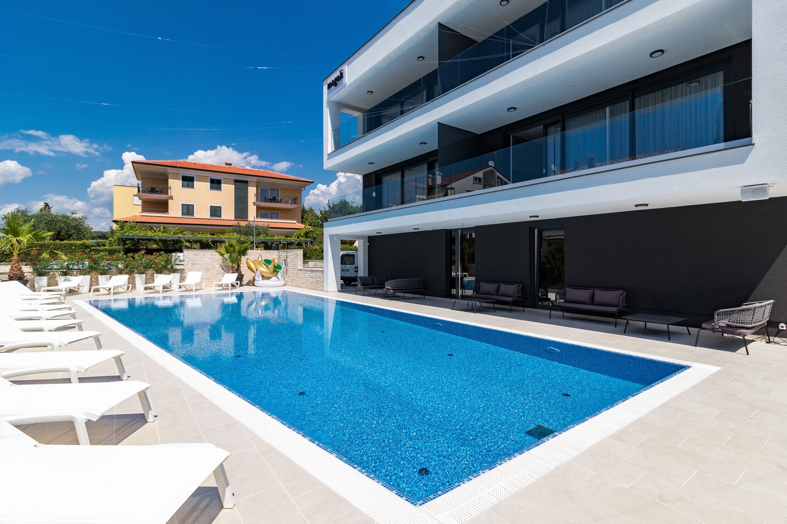 Un hotel moderno con piscina, mobiliario exterior y vista a un edificio cercano.