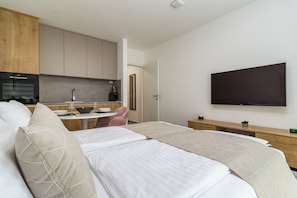 A hotel room with a bed, a TV, a kitchen area, and a dining table.