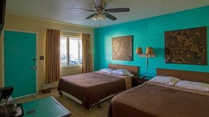 Una camera d'albergo con due letti, una ventola a soffitto, una finestra con tende e opere d'arte alle pareti.