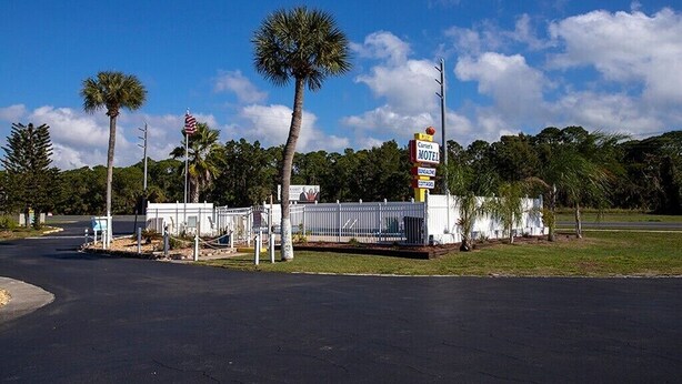 Un motel con un cartello, un'area di parcheggio recintata e palme.