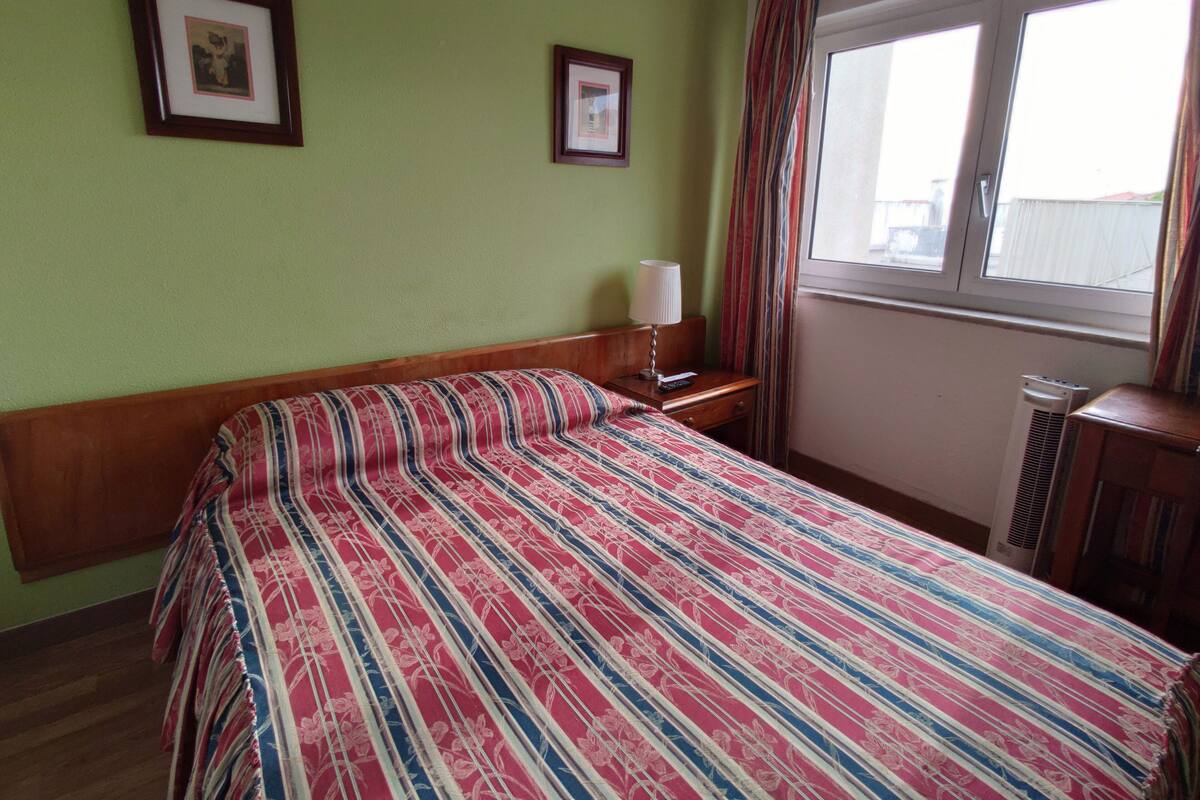 A hotel room with a bed, a nightstand, a lamp, a window with curtains, and two framed pictures on the wall.