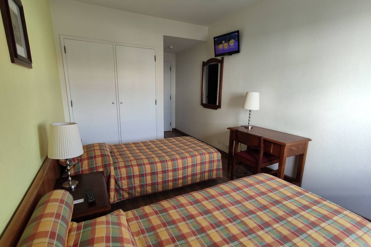 A hotel room with two beds, a desk, a chair, a TV, and a wardrobe.