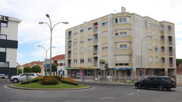 Un hotel de varios pisos con balcones, un patio central con flores y una calle en el frente.