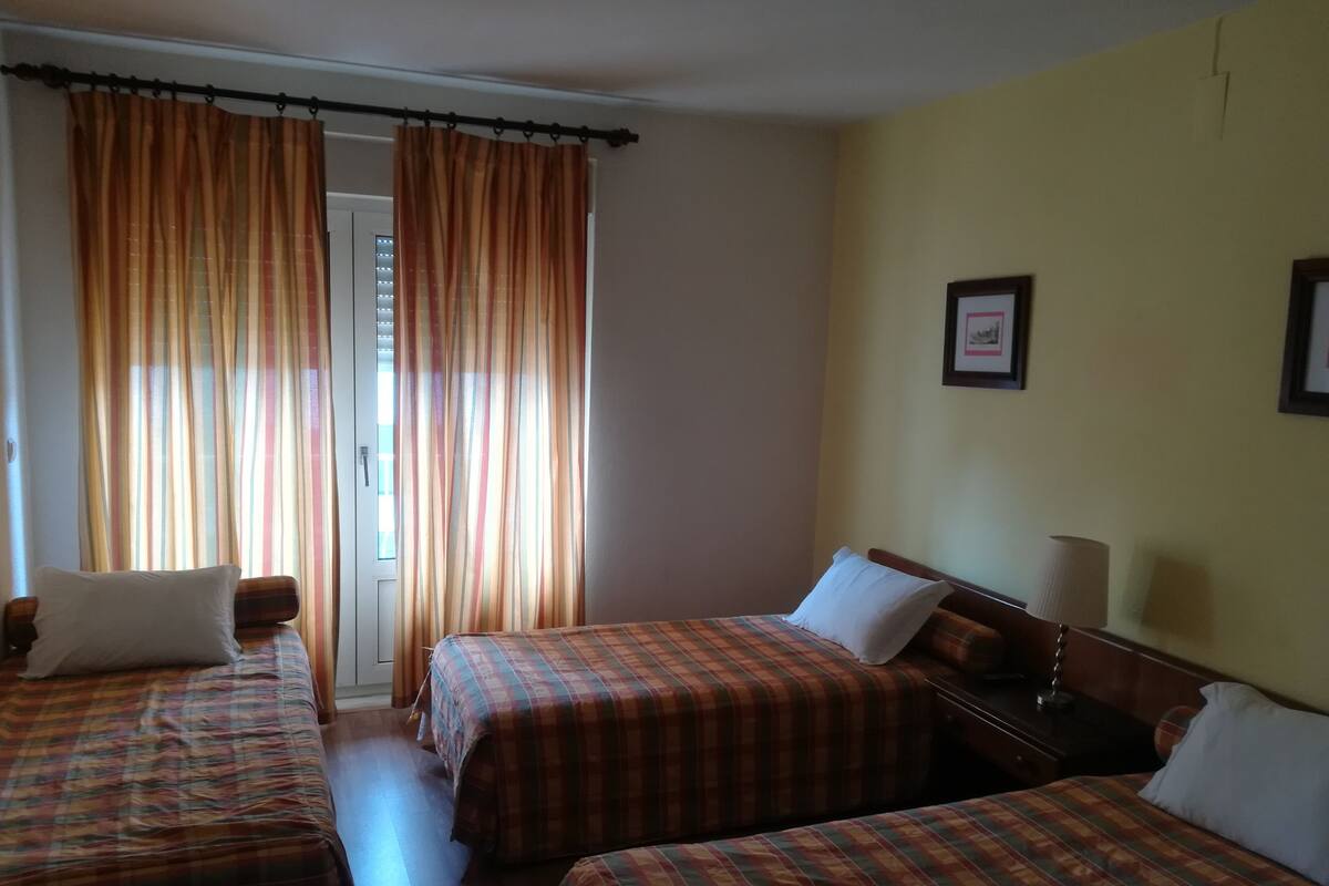 A hotel room with two beds, a nightstand, a lamp, and a door with curtains.