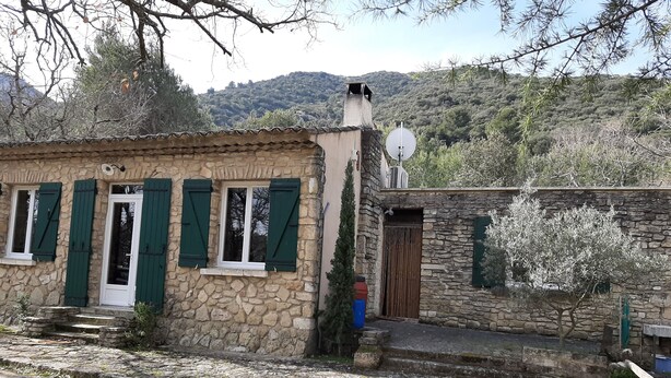 Un bâtiment en pierre avec des volets verts, une antenne parabolique et une vue sur une colline.