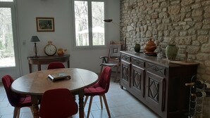 Un coin repas avec une table ronde, des chaises rouges, un mur en pierre et un meuble à vin.