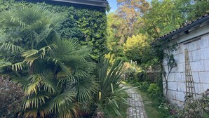 A garden with a stone pathway, lush greenery, and a tiled roof.