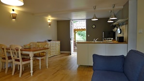 A compact kitchen with a dining area, a blue sofa, and a wooden dining table with chairs.