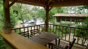 A wooden deck with a table and chairs, overlooking a river and a parked car.
