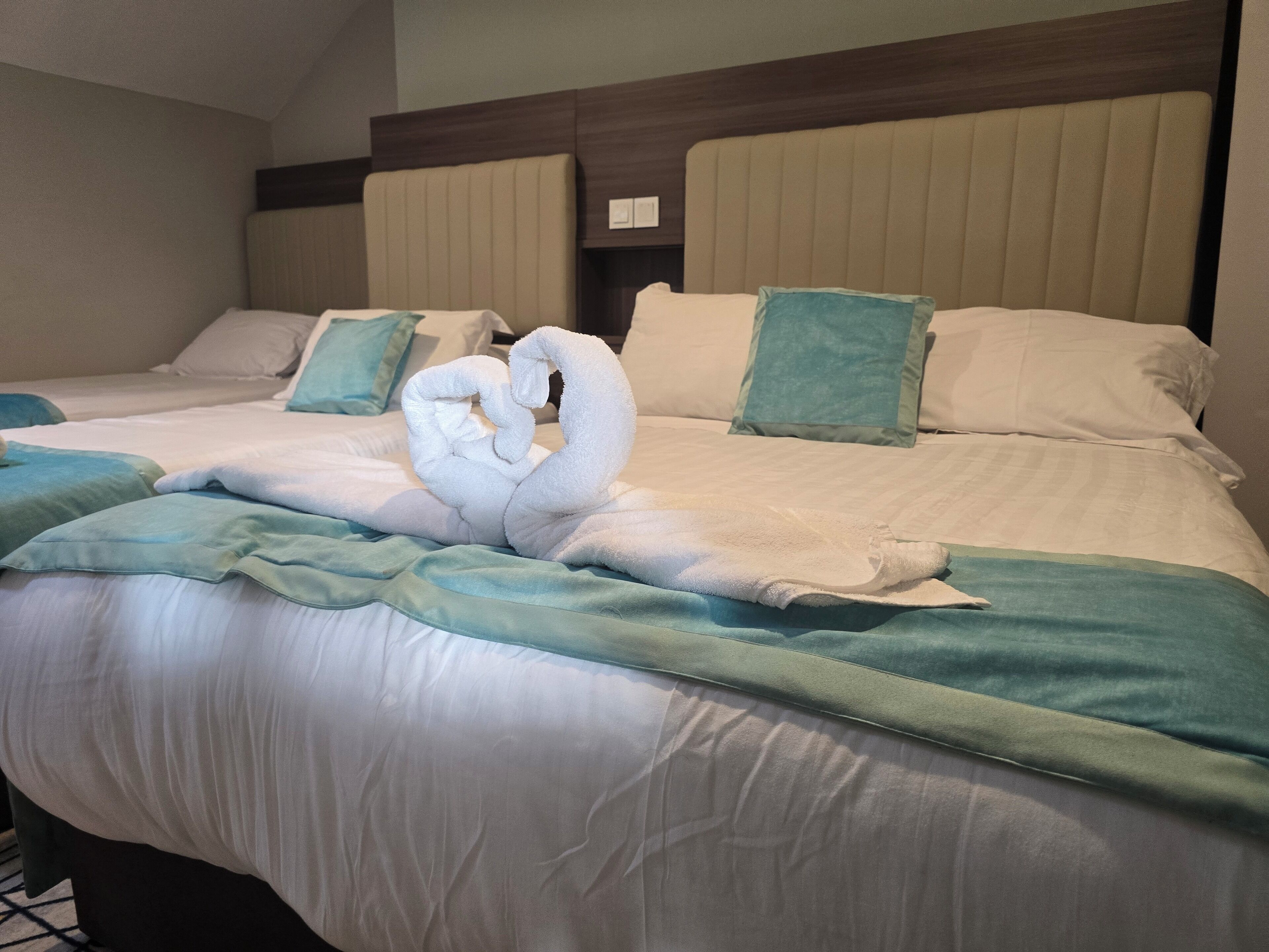 A hotel room with two beds, each with a headboard, and a decorative swan made of towels on the bed.