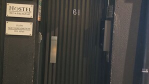 A hotel entrance with a metal door marked with the number 61. There are signs indicating 'KGT HOUSE 61', 'HOSTEL', and 'IRISH ACCOMMODATION'.