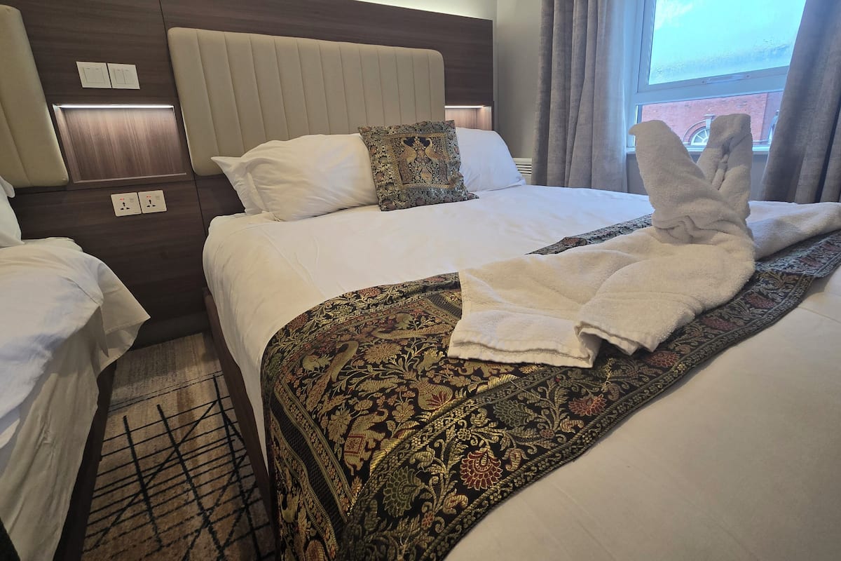 A hotel room with a large bed, a smaller bed, and a sofa bed. There are two bedside tables with lamps and a window with curtains.