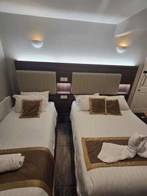 Habitación de hotel con dos camas, cada una con cabecera, lámparas de noche y ventana.