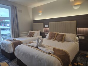 Habitación de hotel con dos camas, cada una con cabecero, ropa de cama blanca y almohadas decorativas marrones. Hay lámparas de pared sobre cada cama.