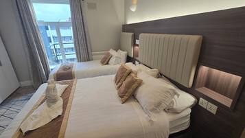 A hotel room with two beds, a large window with curtains, a wall-mounted light, and a view of buildings outside.