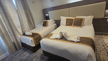 A hotel room with two beds, each with white linens and leopard print accents. There are towels arranged on the beds, and the room has a patterned carpet.