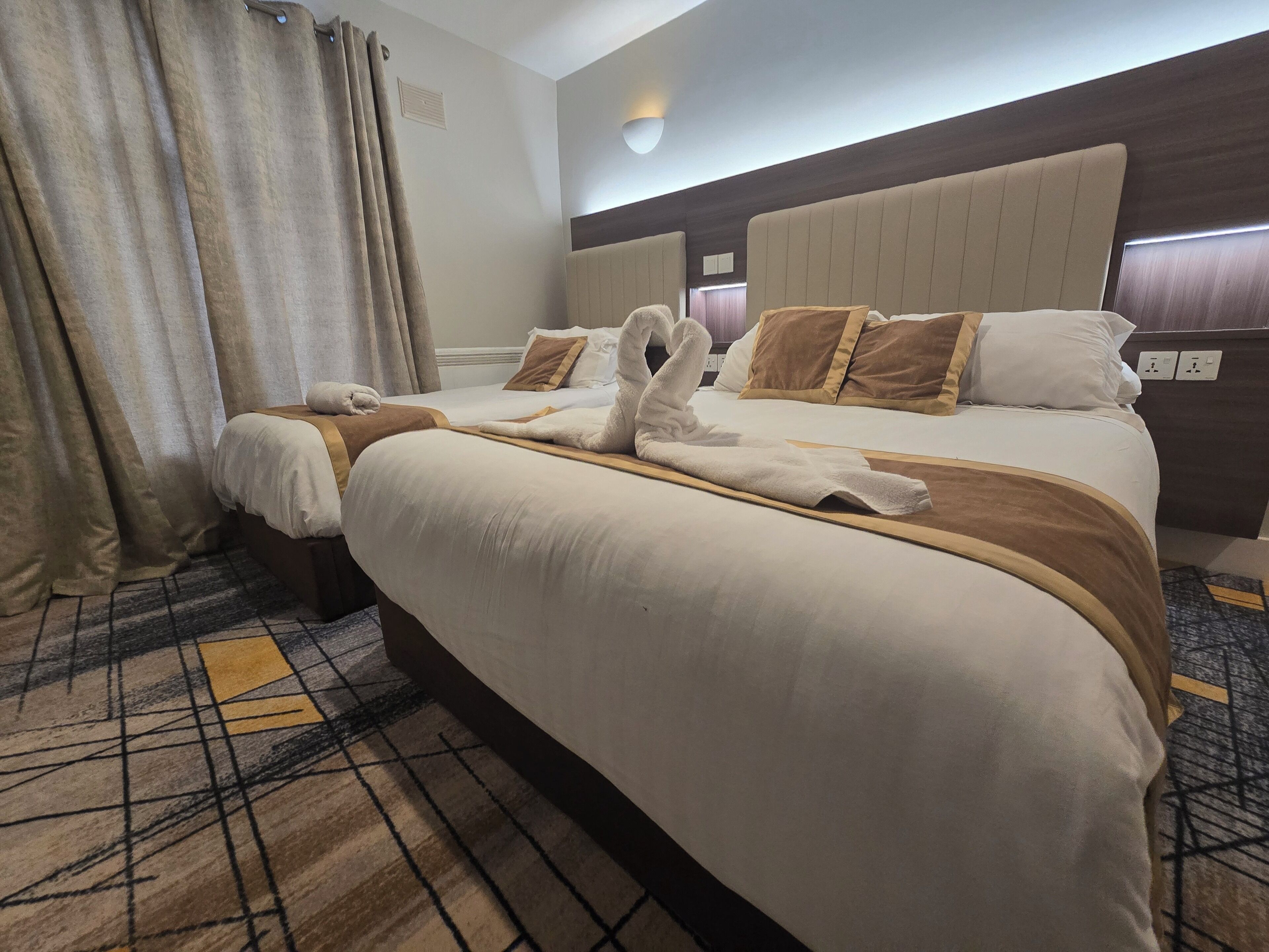 A hotel room with two beds, a large headboard, and a patterned carpet.