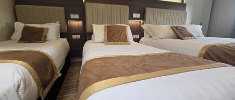 A hotel room with three beds, each with a headboard, white bedding, and brown accent pillows.