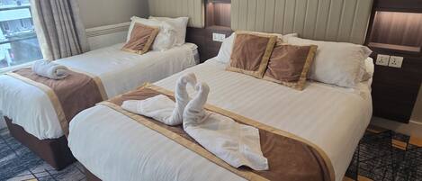 A hotel room with two beds, a large window with curtains, a patterned carpet, and a headboard with built-in lighting.
