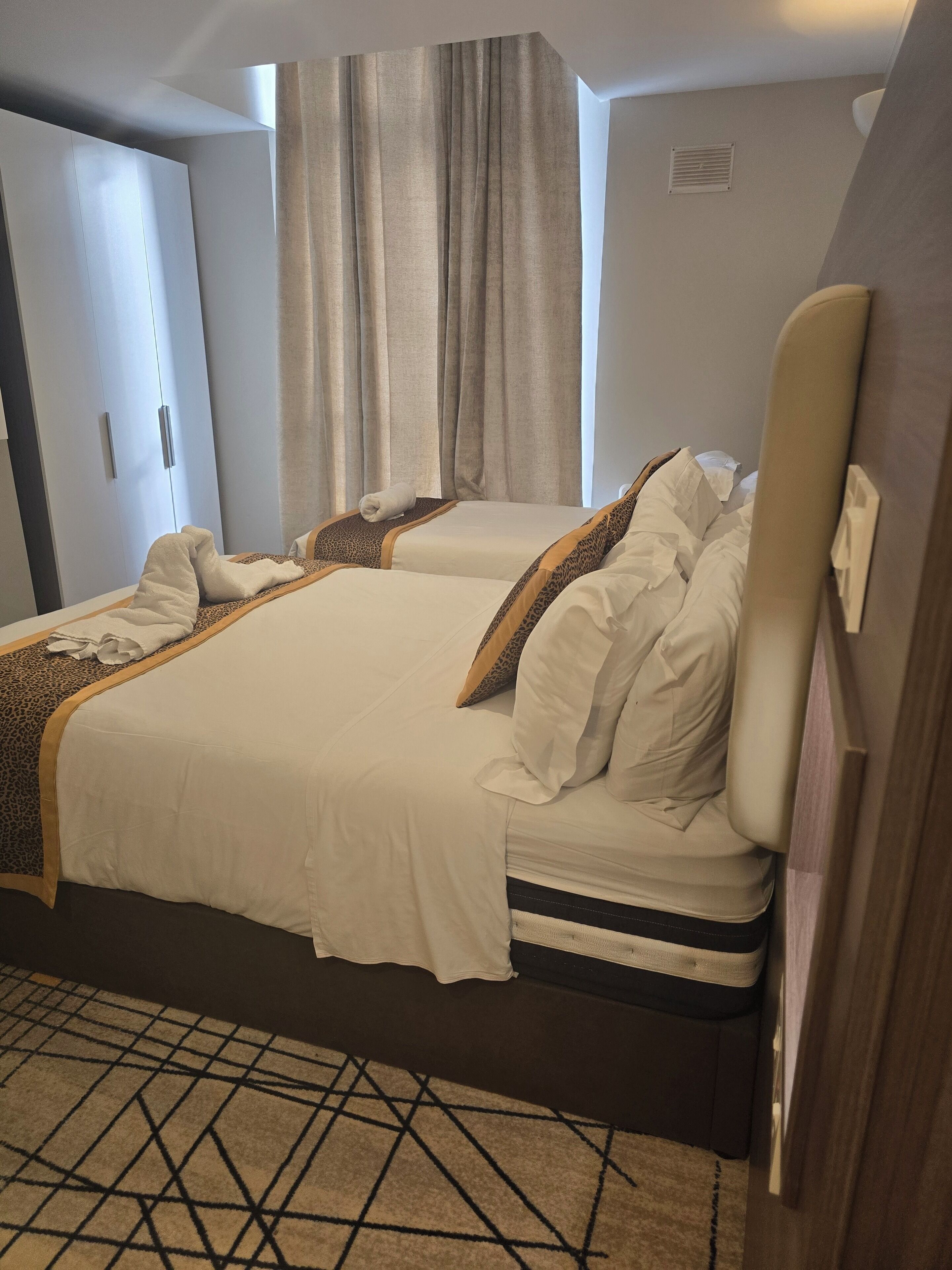 Quarto de hotel com cama, guarda-roupa, janela com cortinas e um tapete estampado.