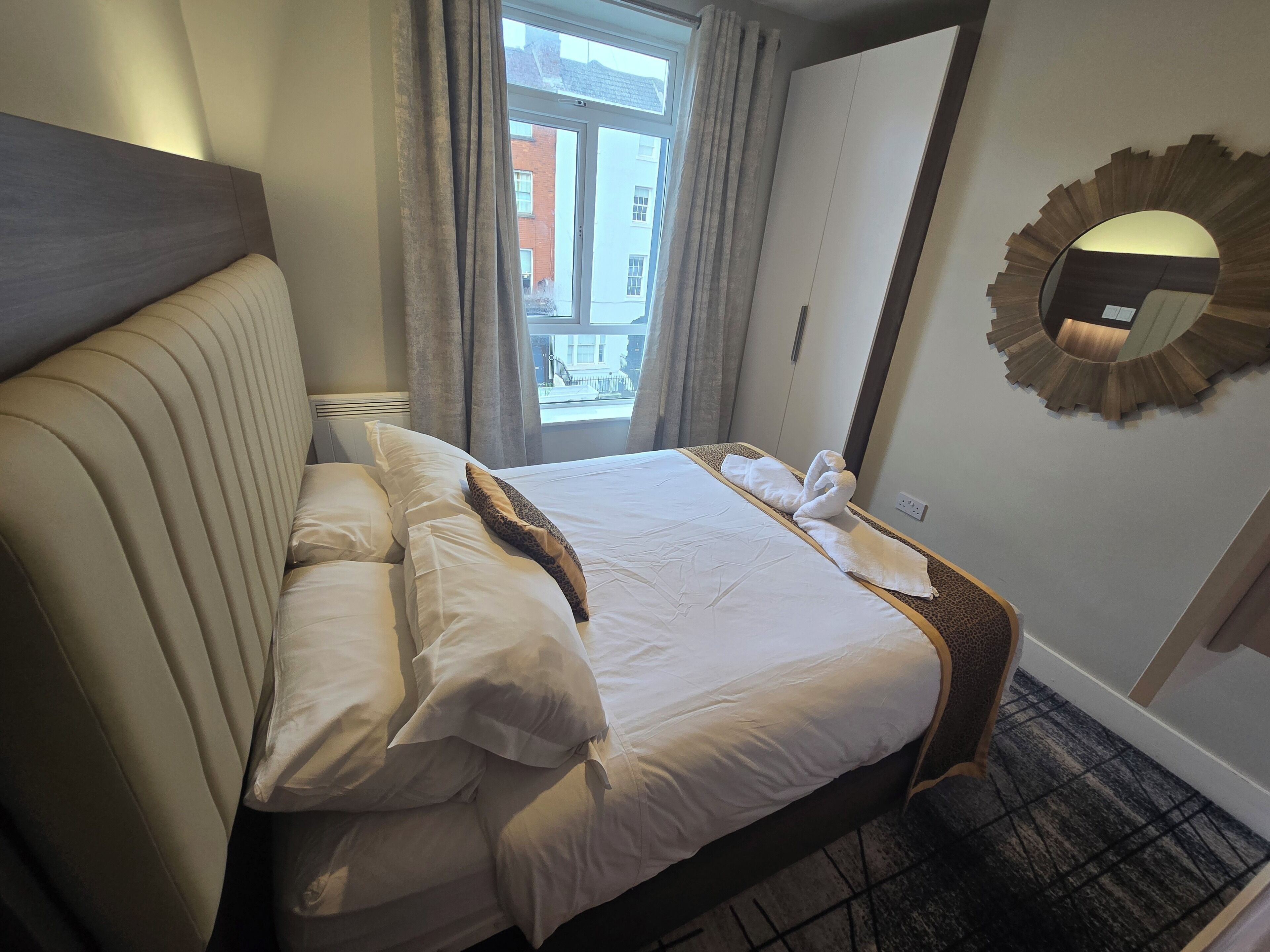 A hotel room with a bed, a mirror, and a view of the outside.