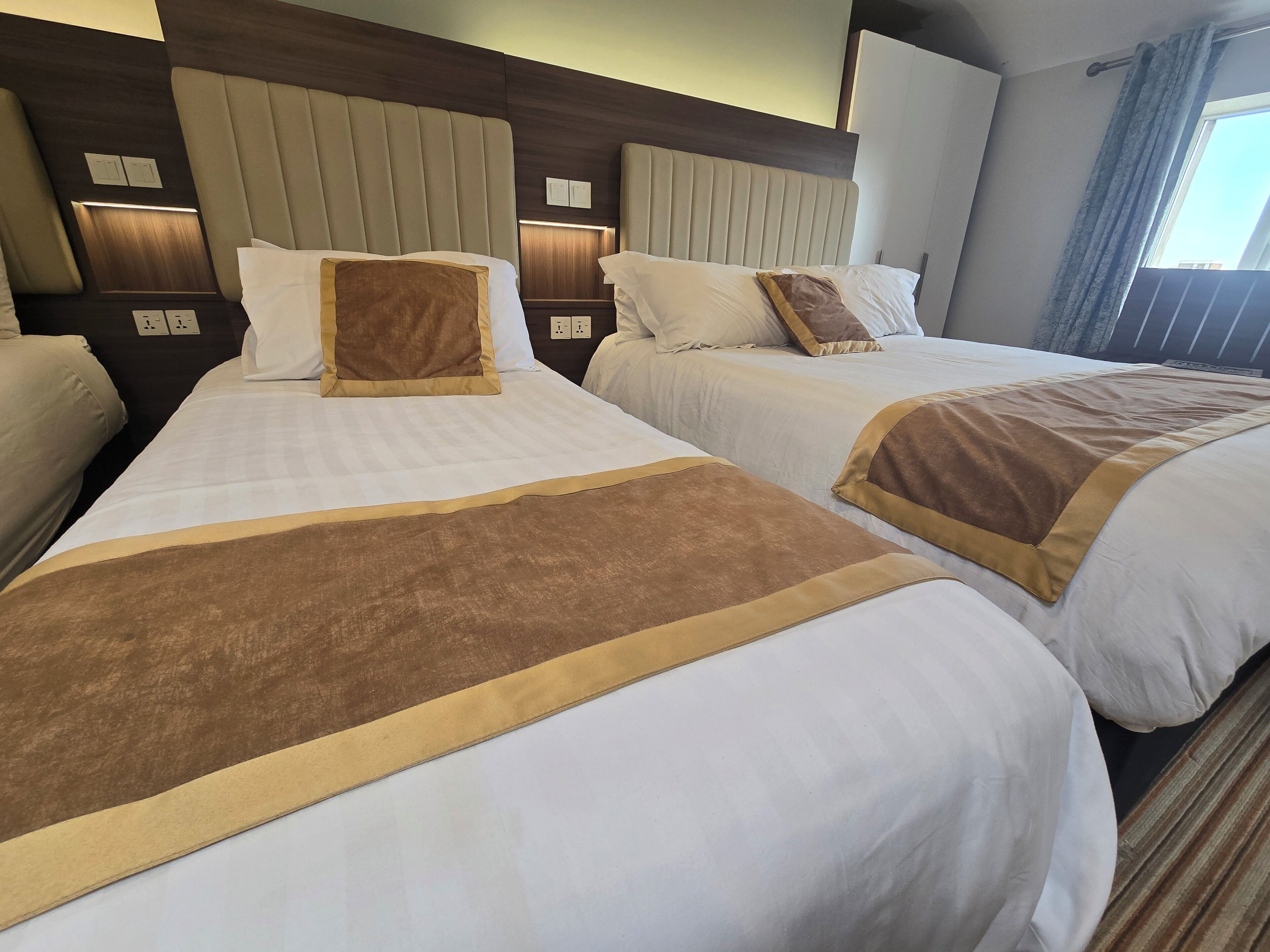 Ett hotellrum med två sängar, var och en med en sänggavel, vita sängkläder och bruna prydnadskuddar.