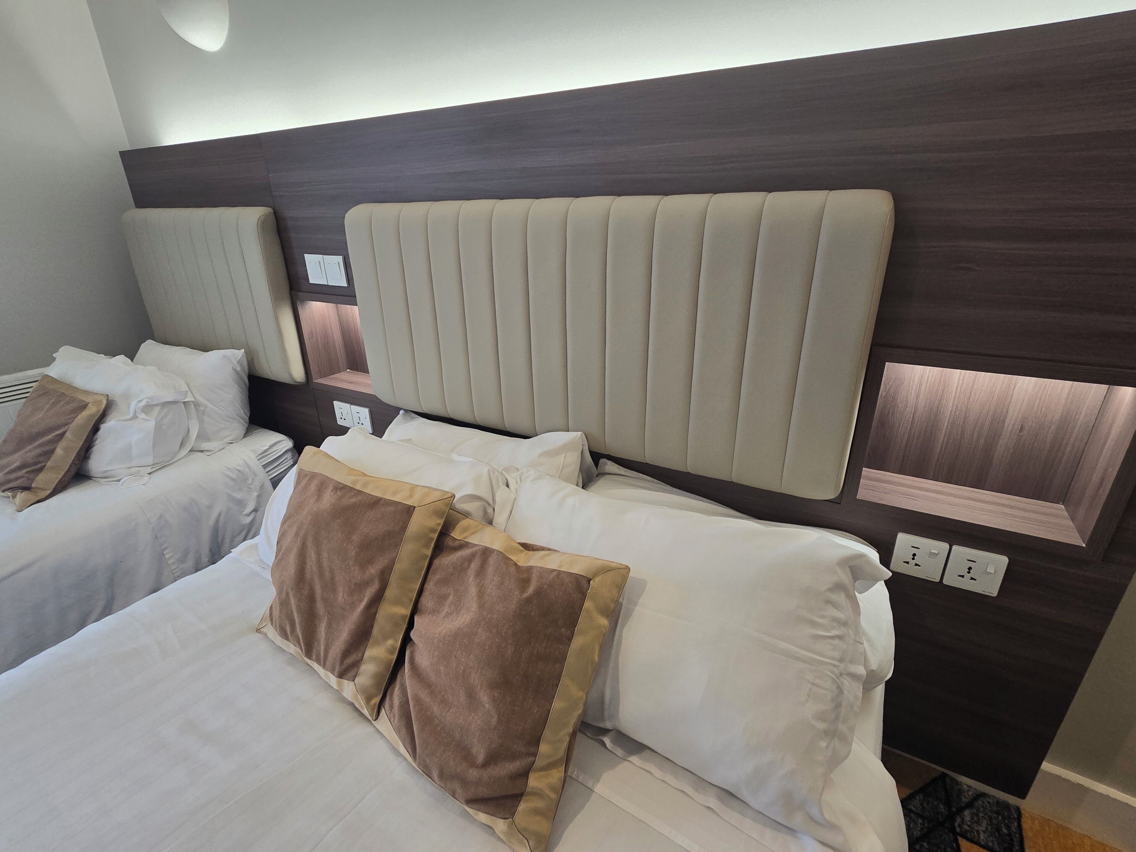 Hotelkamer met twee bedden, elk met hoofdbord, witte beddengoed en bruine sierkussens.