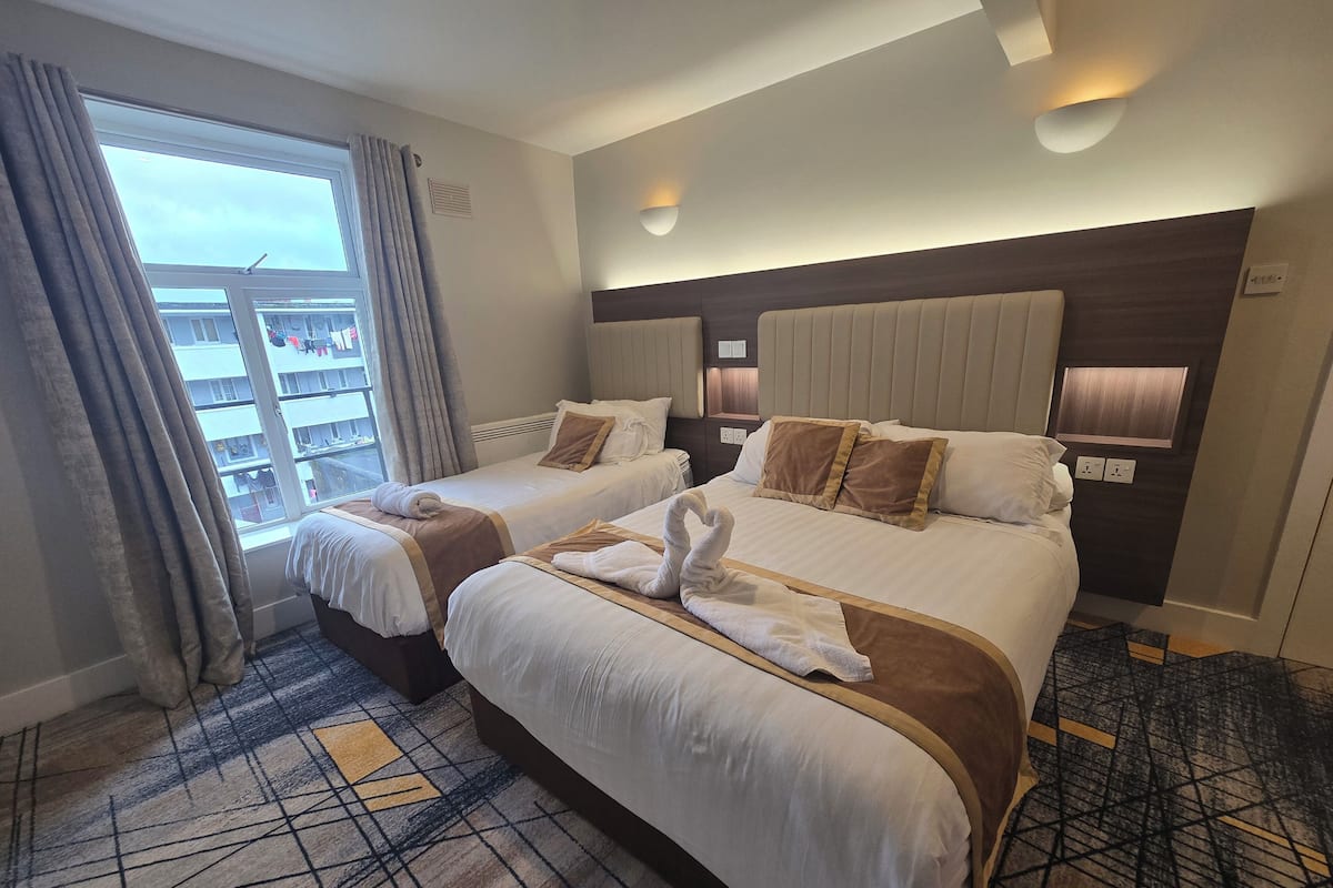 A hotel room with two beds, a large window with curtains, a patterned carpet, and a modern headboard.