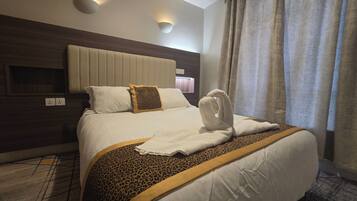 Habitación de hotel con una cama grande, cabecero, luz empotrada en la pared y una ventana con cortinas.