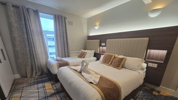 A hotel room with two beds, a large window with curtains, a patterned carpet, and a modern headboard.