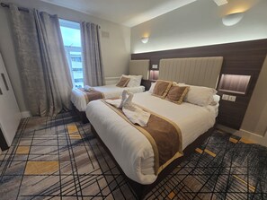 Une chambre d’hôtel avec deux lits, une grande fenêtre avec des rideaux, une moquette à motifs et une tête de lit moderne.