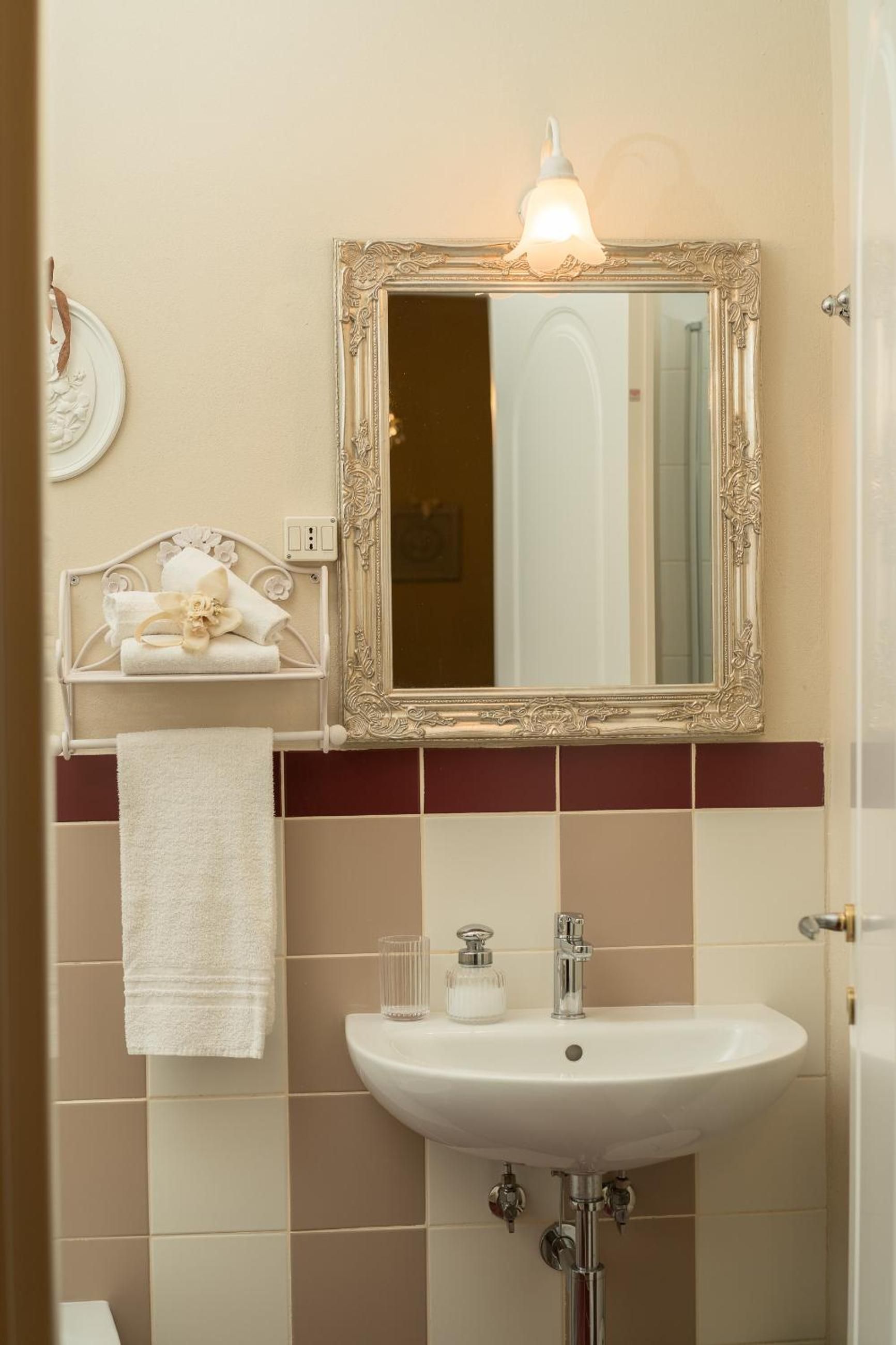 A bathroom with a white sink, a mirror with an ornate frame, and a towel rack with a decorative towel.