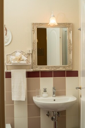 Un baño con un lavamanos blanco, un espejo con un marco ornamentado y un perchero con una toalla decorativa.
