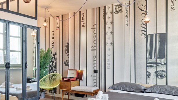 Een moderne hotelkamer met een groot bed, een bureau met stoel, een spiegel, en een wand met verticale strepen en boektitels.