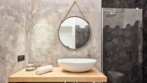 Een badkamer met een ronde spiegel, een houten aanrechtblad, een witte wasbak en een douchegedeelte met honingraat tegels.