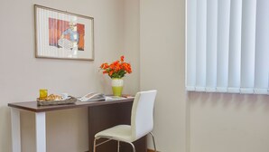 A small dining area with a table, a chair, a vase with flowers, a framed picture, and a window with blinds. - Sturzo 44 (Palermo)