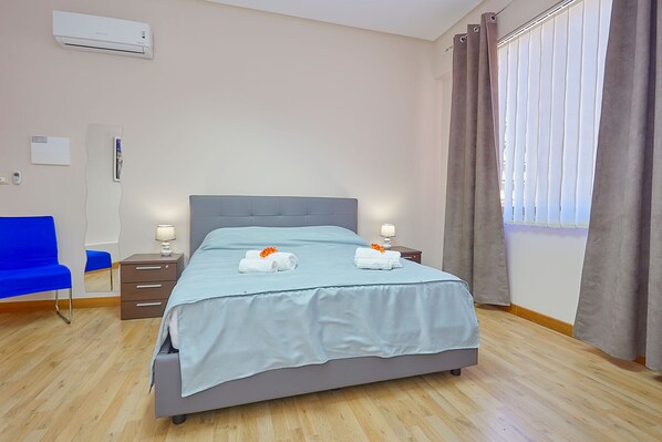 Una habitación de hotel ordenada con cama, mesitas de noche, una silla y ventana con cortinas.