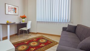 A living room with a grey sofa, a white desk with a chair, a framed picture, a vase with flowers, and a window with blinds. - Sturzo 44 (Palermo)