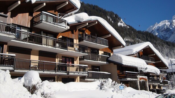 Un hôtel à plusieurs étages, doté de balcons, de toits enneigés et surplombant un paysage montagneux.