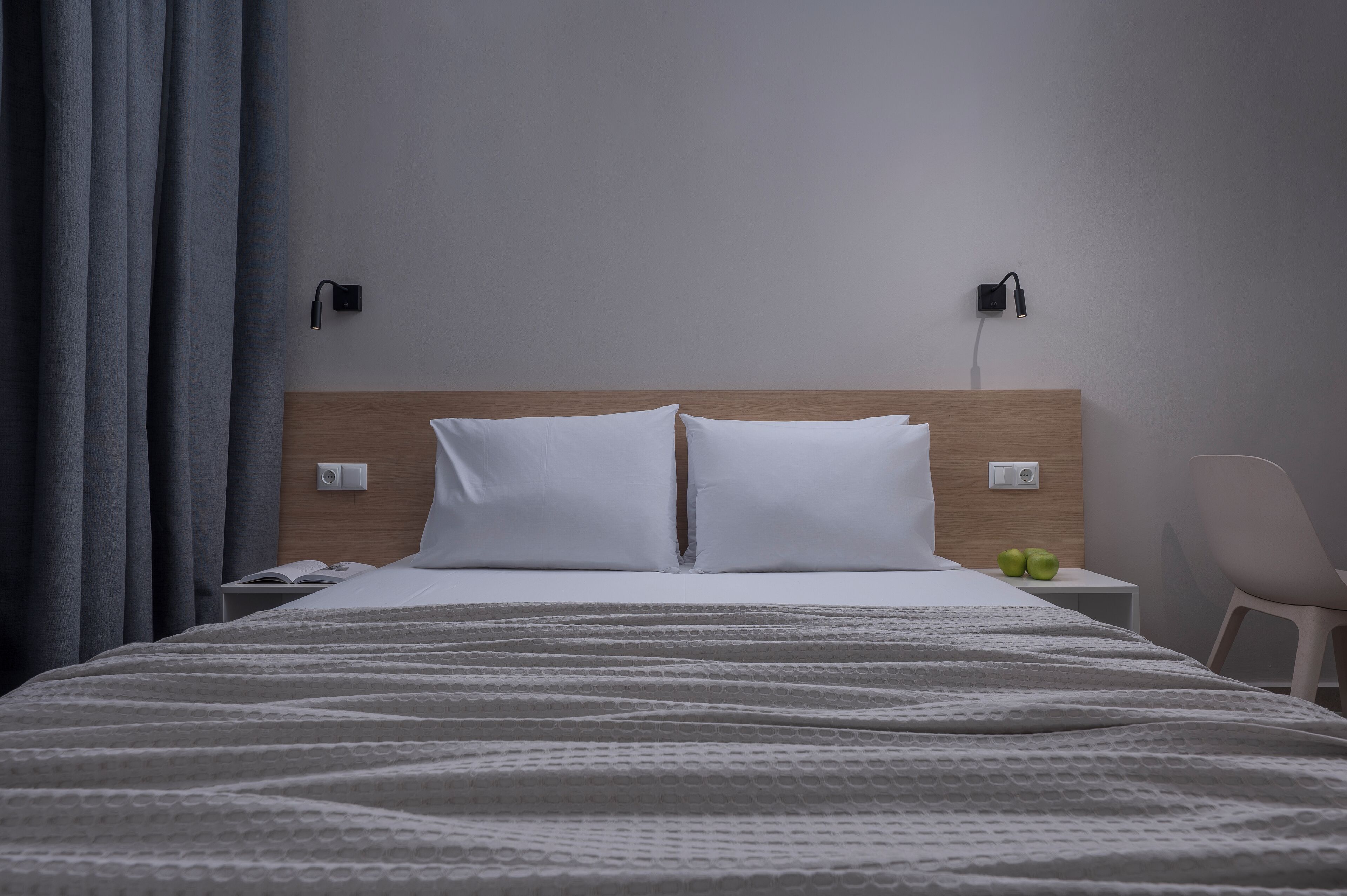 A neatly made bed with white linens, a wooden headboard, and two bedside lamps.