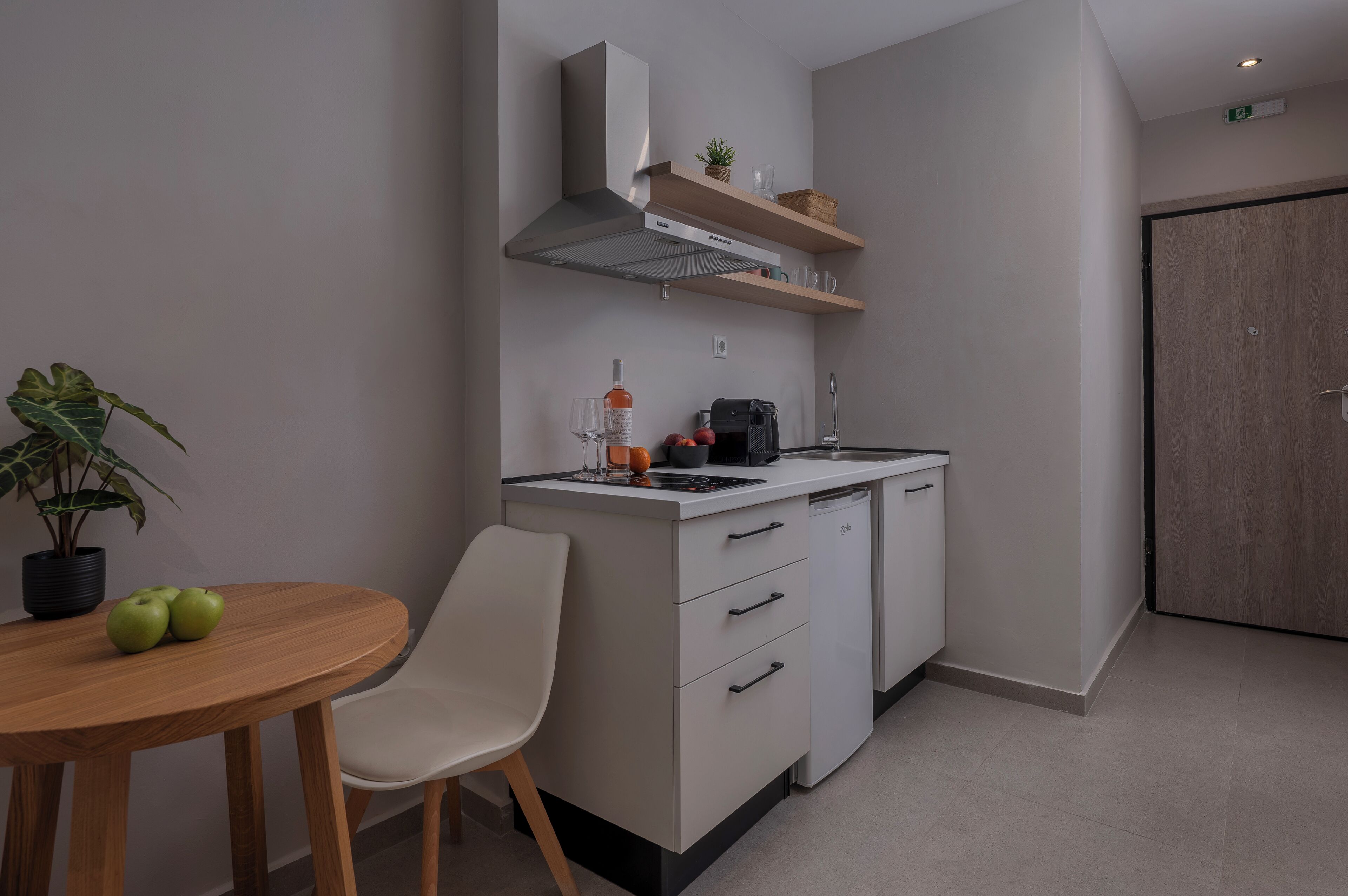 Una cocina compacta con estufa integrada, microondas y una pequeña encimera. Hay una silla y una mesa con manzanas encima.