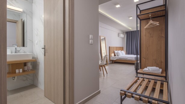 Quarto de hotel moderno com banheiro, uma cama, um banco de madeira e um cabideiro.