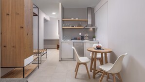 Uma cozinha moderna com armários brancos, fogão embutido e uma área de jantar com duas cadeiras brancas e uma mesa de madeira.