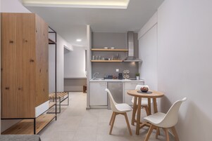 A modern kitchen with white cabinets, a built-in stove, and a dining area with two white chairs and a wooden table.