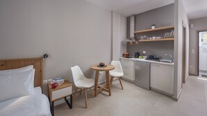 Quarto de hotel compacto com cama, uma pequena mesa de jantar com cadeiras, cozinha compacta com pia e armários, e uma janela.
