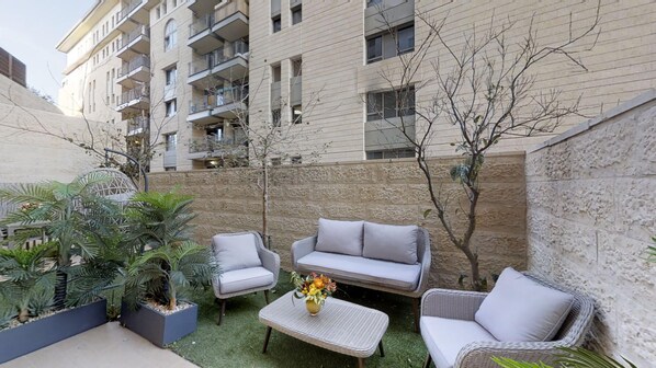 Un espace extérieur aménagé avec des meubles en osier et une petite table, entouré de plantes en pot et d’un mur de pierre.
