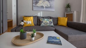 A modern living room with a grey sofa, yellow and patterned cushions, a white coffee table with a tray holding plants, and a framed artwork of a tree. - Cozy Apartment in Syntagma - Plaka by GHH (Athens)