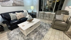 Una sala de estar con un sofá de cuero negro, una mesa de centro blanca, un tapete mullido gris y un sillón de cuero marrón.