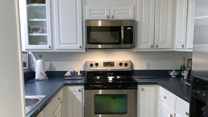 Una cocina moderna con armarios blancos, una estufa de acero inoxidable, un microondas y un refrigerador.