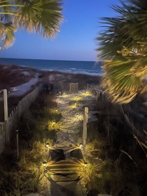 Ein Strandweg führt zum Meer, umgeben von Holzzäunen und Palmen.